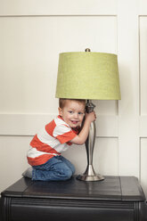 Portrait of boy holding and playing with lamp shade on table - CAVF12485