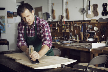 Mann sägt Holz, während er in der Werkstatt eine Geige baut - CAVF12504