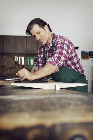 Lächelnder Mann sägt Holz in einer Werkstatt, lizenzfreies Stockfoto