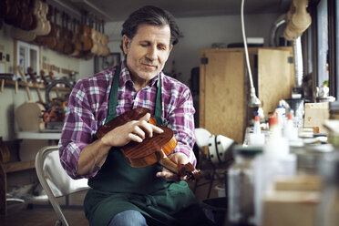 Arbeiter, der bei der Arbeit in der Werkstatt eine Geige berührt - CAVF12508