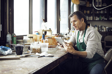 Man using tablet computer while sitting in workshop - CAVF12514