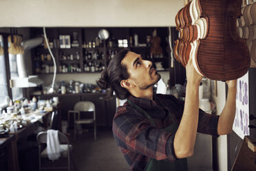 Arbeiter, der in der Werkstatt stehend eine Geige aufhängt - CAVF12519