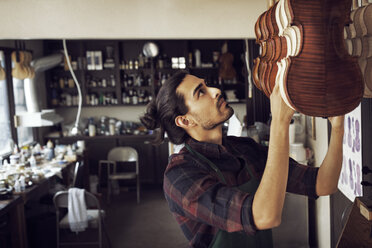 Worker hanging violin while standing in workshop - CAVF12519