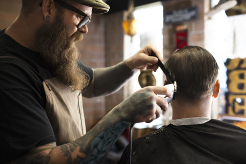 Friseur schneidet einem Mann die Haare mit einem elektrischen Rasiermesser im Geschäft, lizenzfreies Stockfoto