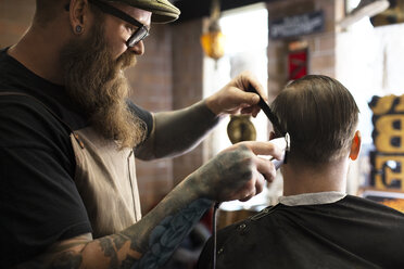 Friseur schneidet einem Mann die Haare mit einem elektrischen Rasiermesser im Geschäft - CAVF12549