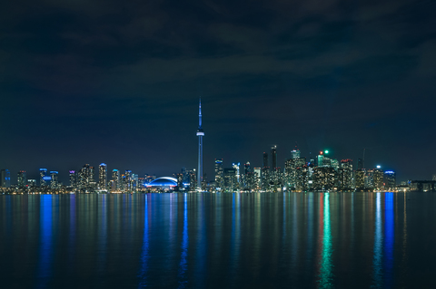 Illuminated modern buildings reflecting in lake Ontario against sky at night stock photo