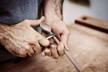 Mittelteil eines Schreiners, der in einer Werkstatt einen Holzlöffel mit einem Messer schnitzt - CAVF12566
