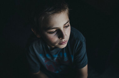 High angle view of thoughtful boy sitting in dark room - CAVF12584