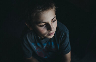 Hoher Blickwinkel auf einen nachdenklichen Jungen, der in einem dunklen Raum sitzt - CAVF12584