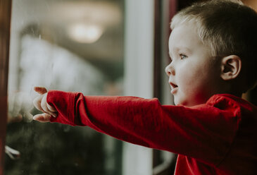 Seitenansicht eines Jungen, der durch ein Fenster schaut, während er zu Hause steht - CAVF12608
