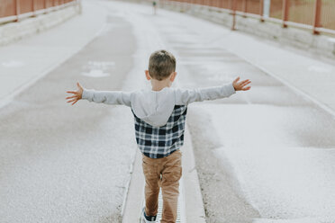 Rear view of boy with arms outstretched walking on street - CAVF12609