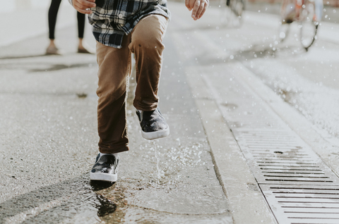 Niedriger Ausschnitt eines Jungen, der auf eine Pfütze an der Straße springt, lizenzfreies Stockfoto