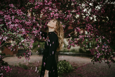 Blütenblätter fallen auf eine Frau, die unter einem blühenden Baum im Park steht, lizenzfreies Stockfoto