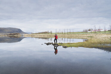 Mann fotografiert am Seeufer stehend gegen bewölkten Himmel - CAVF12763