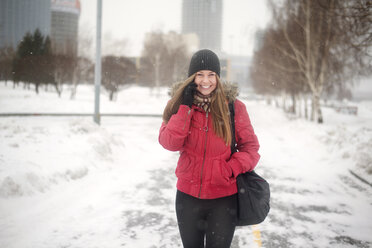 Glückliche junge Frau, die mit ihrem Handy telefoniert, während sie im Winter auf der Straße spazieren geht - CAVF12776