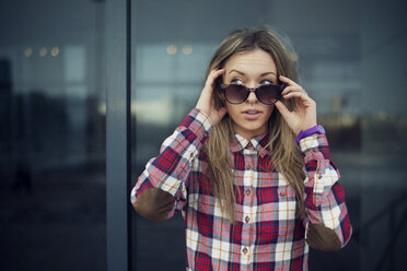 Beautiful woman holding sunglasses while looking away against building - CAVF12785