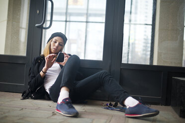 Female hipster using phone while relaxing against door - CAVF12789