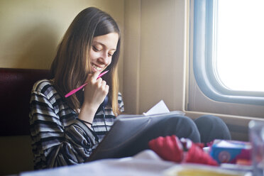 Lächelnde Frau, die ein Buch betrachtet, während sie im Zug reist - CAVF12834
