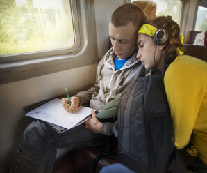 Woman looking at sketch while relaxing on friend's shoulder in train - CAVF12837