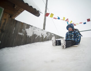 Glücklicher Junge beim Schlittenfahren auf einem schneebedeckten Hügel - CAVF12861
