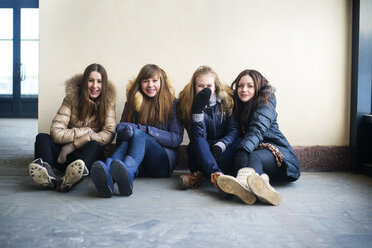 Portrait of happy friends sitting against wall - CAVF12866