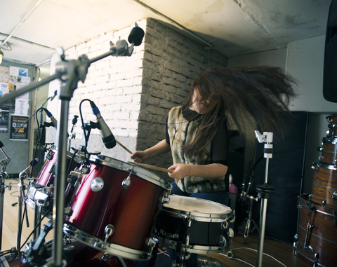 Happy woman enjoying while playing drum kit at home stock photo