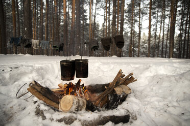 Essen wird in Behältern über Lagerfeuer auf einem schneebedeckten Feld im Wald gekocht - CAVF12875
