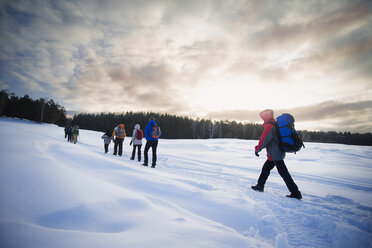 Freunde wandern auf schneebedecktem Feld gegen bewölkten Himmel - CAVF12880