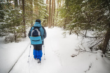 Rückansicht eines Wanderers, der einen Rucksack trägt, während er durch einen schneebedeckten Wald läuft - CAVF12891