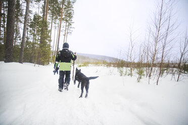 Rückansicht eines Jungen mit Hund, der auf einem schneebedeckten Feld gegen den Himmel läuft - CAVF12892