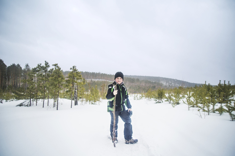 Porträt eines Jungen, der einen Stock hält, während er auf einem schneebedeckten Feld vor einem klaren Himmel steht, lizenzfreies Stockfoto