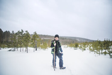 Porträt eines Jungen, der einen Stock hält, während er auf einem schneebedeckten Feld vor einem klaren Himmel steht - CAVF12893