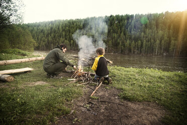 Vater und Sohn machen ein Lagerfeuer auf einer Wiese am Fluss - CAVF12911