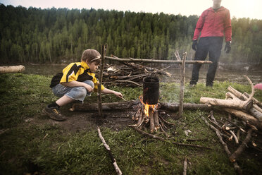 Junge bereitet mit seinem Vater auf dem Campingplatz Essen am Lagerfeuer zu - CAVF12912