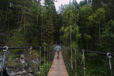 Rückansicht eines Mannes, der auf einer Brücke inmitten von Bäumen im Wald geht - CAVF12928