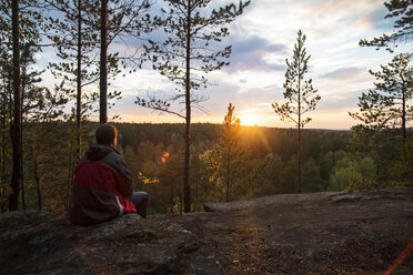 Rückansicht eines auf einem Felsen sitzenden Mannes gegen den Himmel bei Sonnenuntergang - CAVF12966