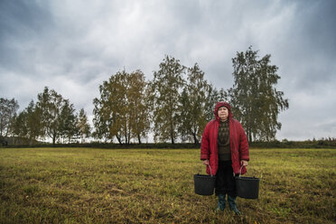 Porträt einer Landarbeiterin, die Eimer hält, während sie auf einem Feld vor einem bewölkten Himmel steht - CAVF12972