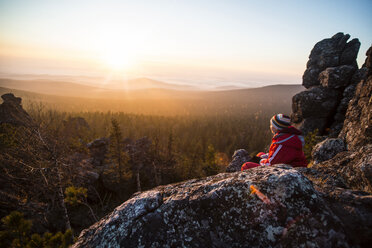 Frau sitzt auf Felsen am Berg gegen den Himmel bei Sonnenuntergang - CAVF12979