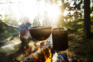 Food being cooked in utensils over bonfire on sunny day - CAVF12981