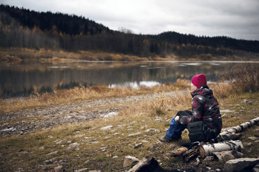 Woman sitting on log at lakeshore - CAVF12982