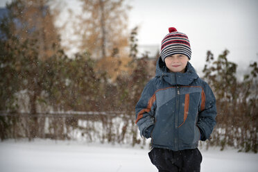 Porträt eines lächelnden Jungen in warmer Kleidung auf einem schneebedeckten Feld - CAVF12998