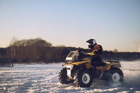 Mann fährt Quad auf schneebedecktem Feld gegen klaren Himmel, lizenzfreies Stockfoto