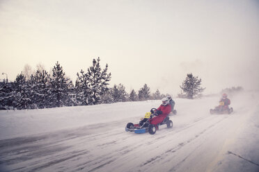 Teenagers racing on go-carts at snow covered field against sky - CAVF13016