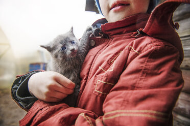 Mittelteil eines Jungen, der ein Kätzchen auf einem Feld trägt - CAVF13035