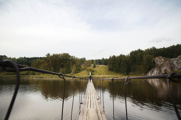 Distant view of man walking on footbridge over lake against sky - CAVF13041