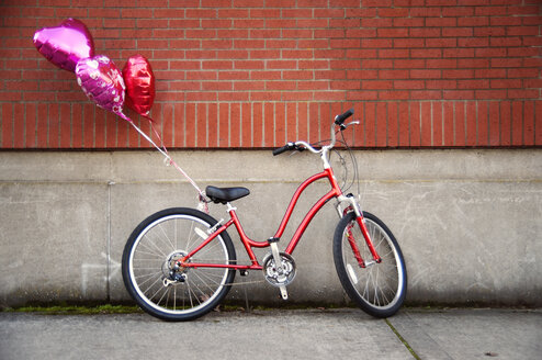 Heart shaped balloons tied to bicycle parked against wall - CAVF13068