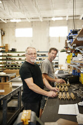 Portrait of smiling workers standing by table in warehouse - CAVF13114