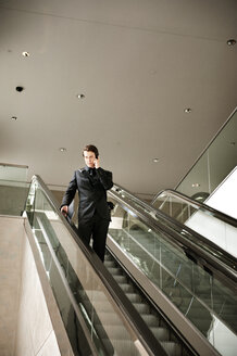 Niedriger Blickwinkel eines Geschäftsmannes, der auf einer Rolltreppe steht und telefoniert - CAVF13124