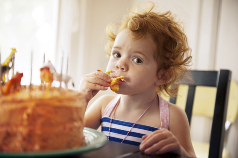 Porträt eines Mädchens, das am Tisch sitzend Kuchen isst, lizenzfreies Stockfoto