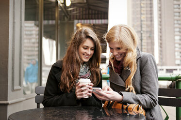 Happy friends using phone while sitting at sidewalk cafe - CAVF13184